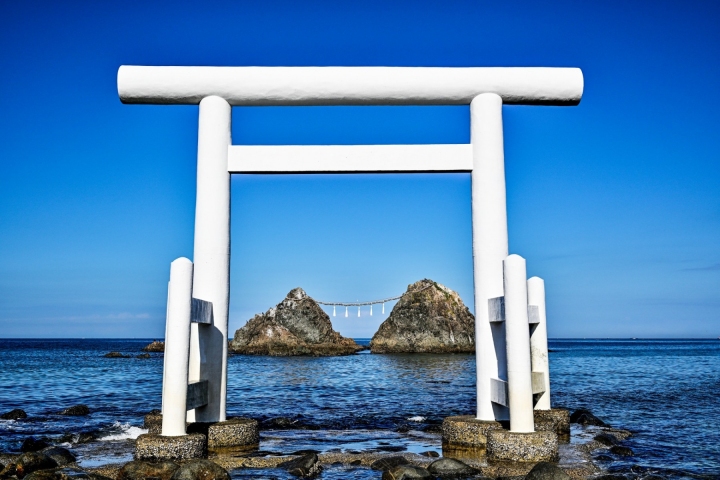 白色鳥居立在海邊，遠方雙岩映襯藍天