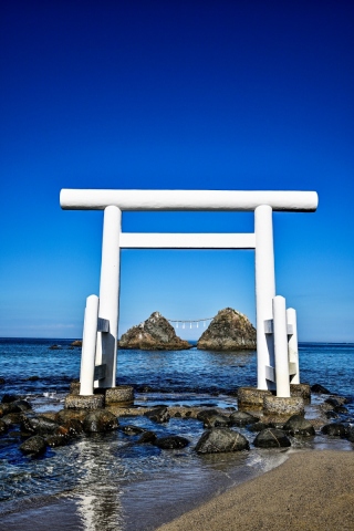 從白色鳥居正面望向蔚藍海面與雙岩