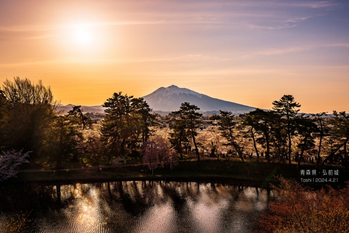 夕陽下的城樓與遠山，前方水面映出樹影